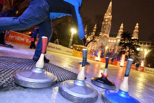 Symbolbild einer Person beim Eisstockschießen. Im Hintergrund ist das festlich beleuchtete Wiener Rathaus während des Wiener Eistraums zu sehen.